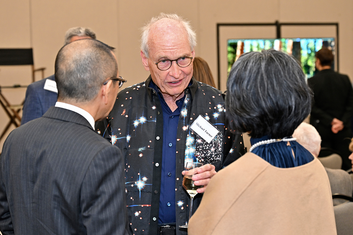 A person in a space themed scarf speaks to colleagues at a reception.