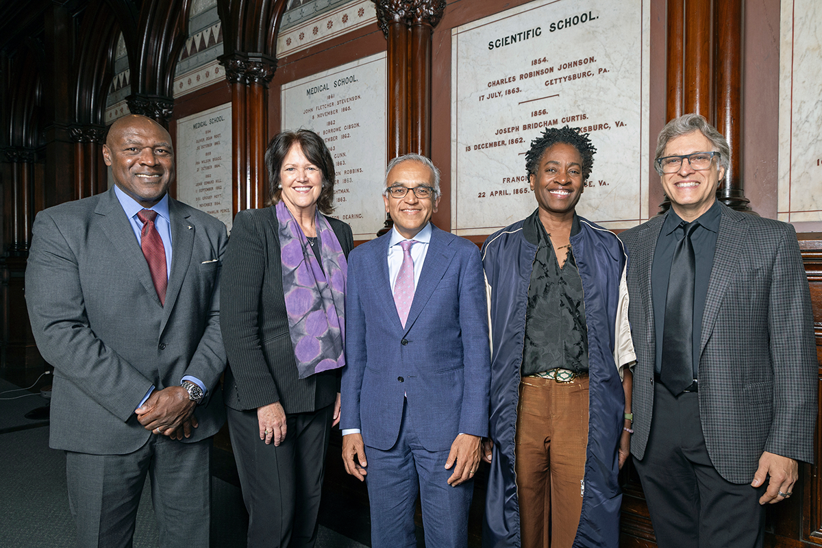 Five formally dressed adults pose and smile against a marble and dark wood background. 