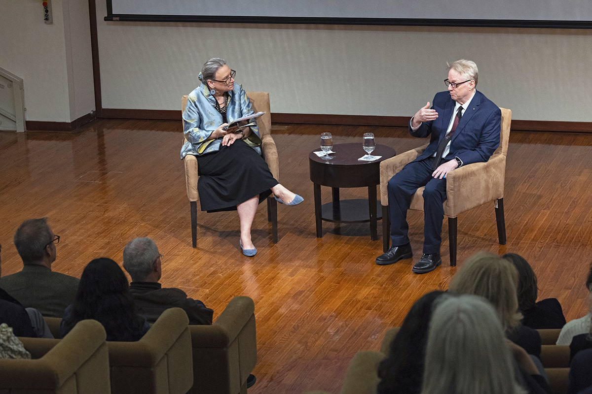 Two formally dressed adults seated on stage in conversation. 