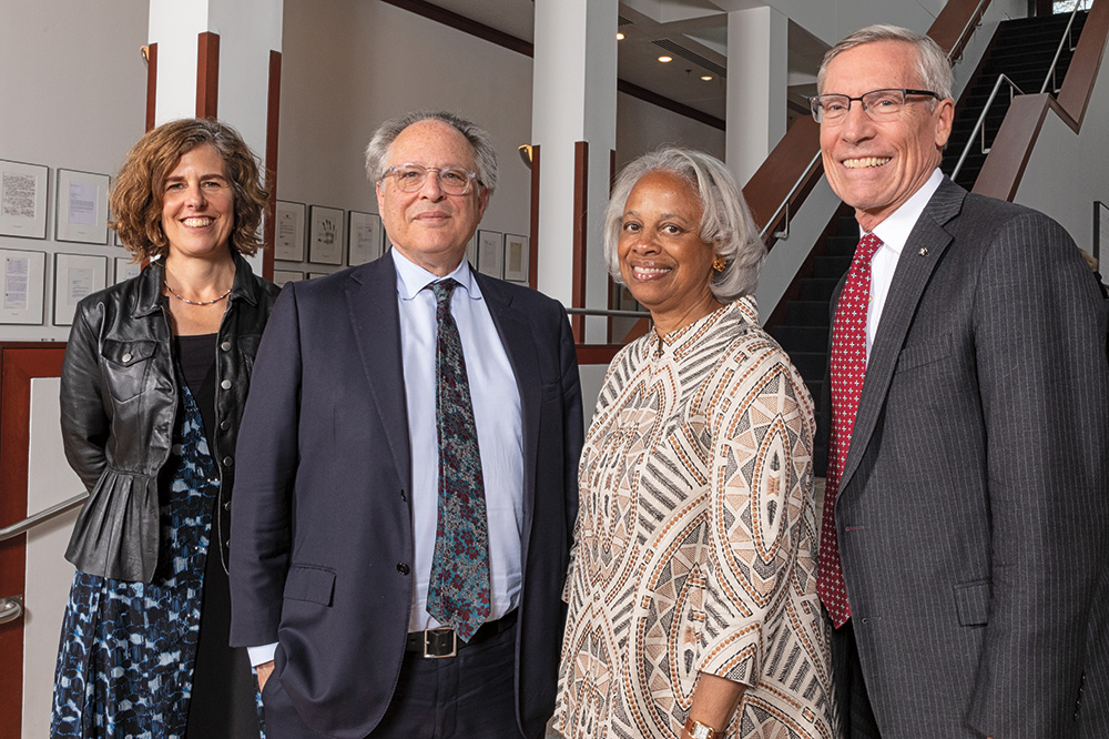 Four individuals standing in the lobby of the American Academy of Arts and Sciences. They wear formal clothing, face the viewer, and smile. 