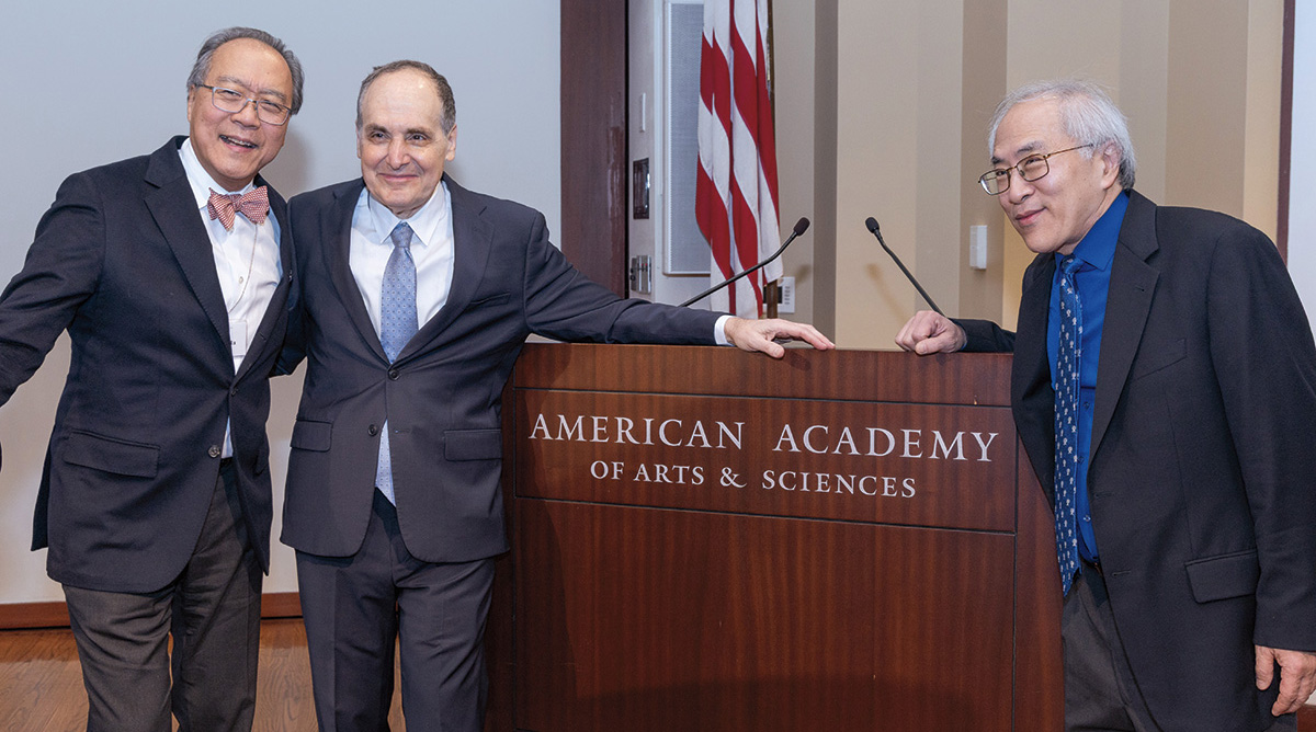 A photo of Yo-Yo Ma, Richard Kogan, and Lynn Chang, all wearing business suits, smiling and posing in front of a podium that says American Academy of Arts & Sciences.