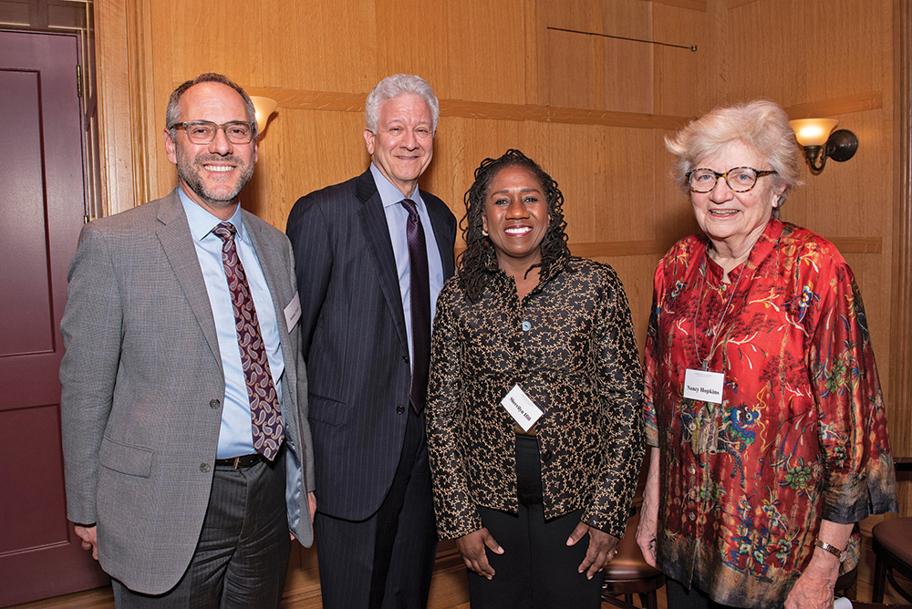 Four people in formal attire face the viewer and smile.