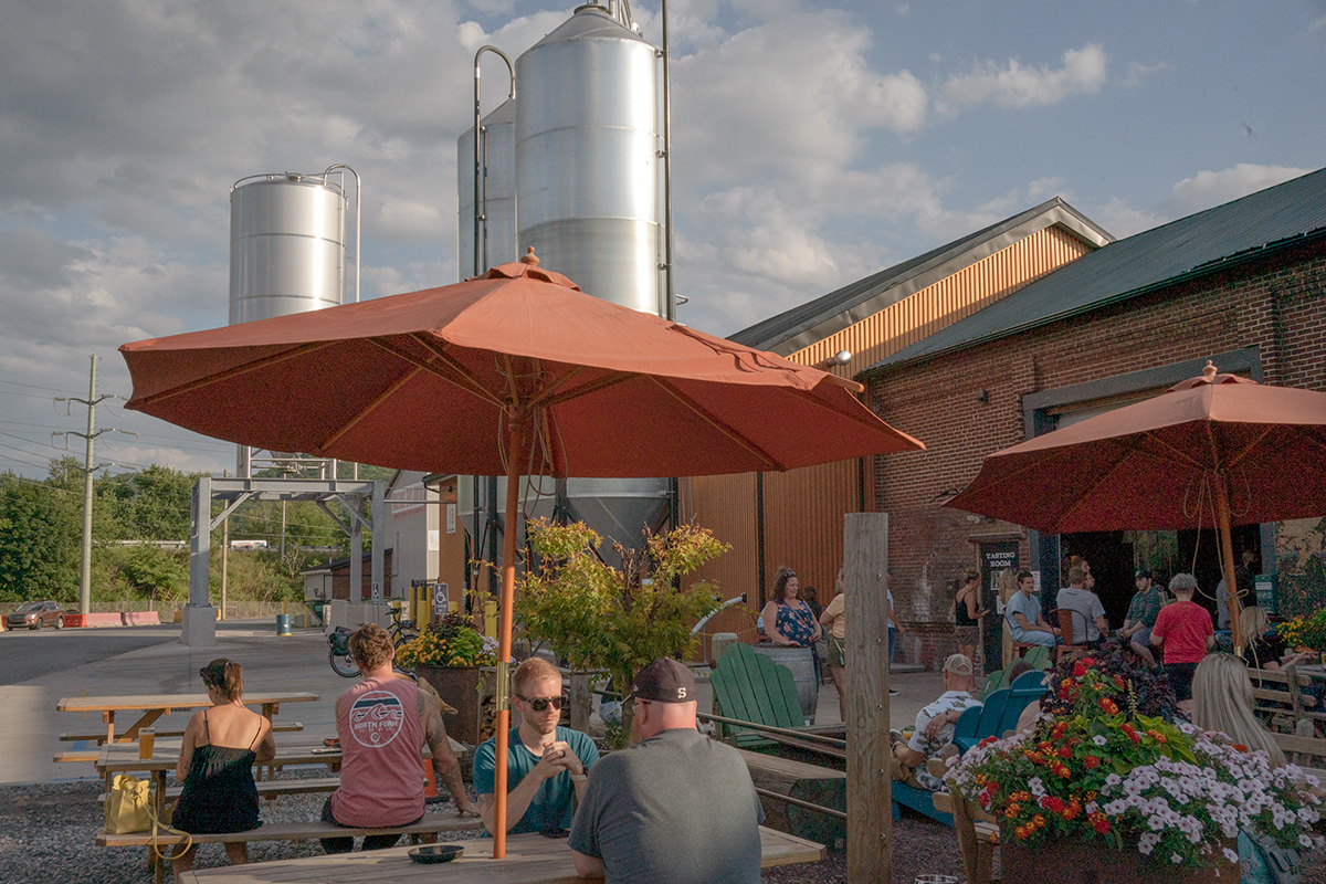 A group of people sitting outside a brewery under umbrellas.