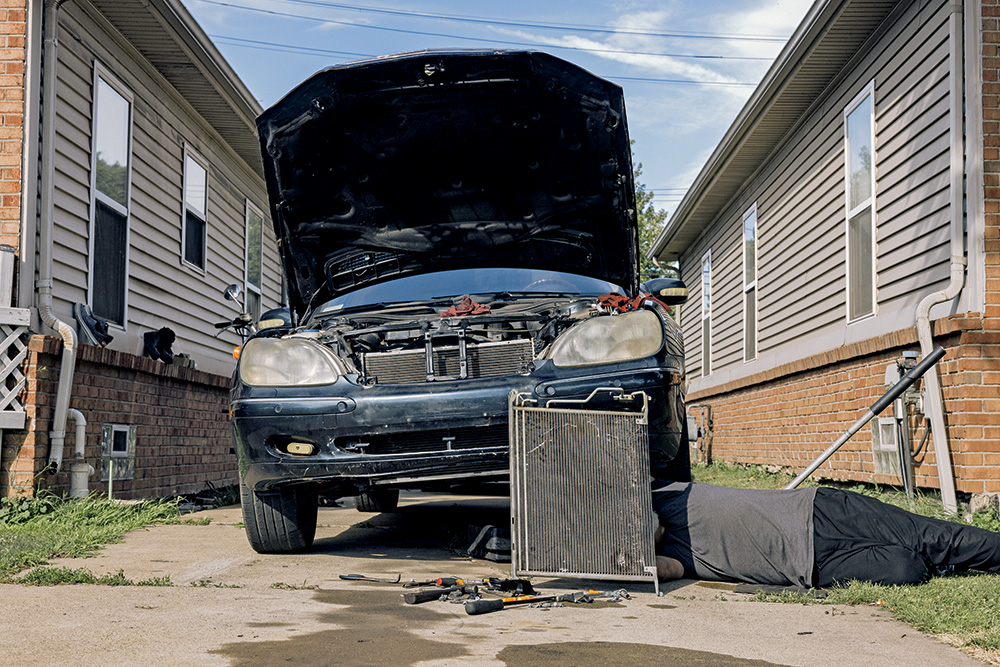 A person working under a car in a driveway. Their face is not visible. 