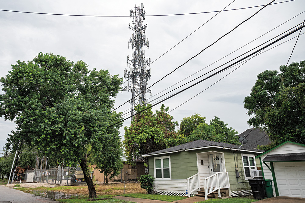 A green and white house sits below powerlines. Green trees are behind and in front of the house. 