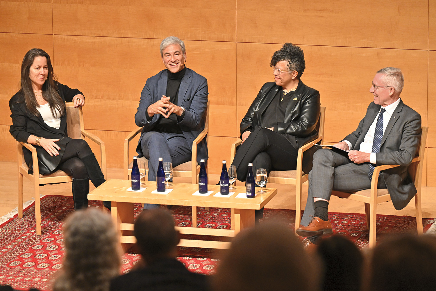 Four people sitting in chairs and smiling in front of an audience.