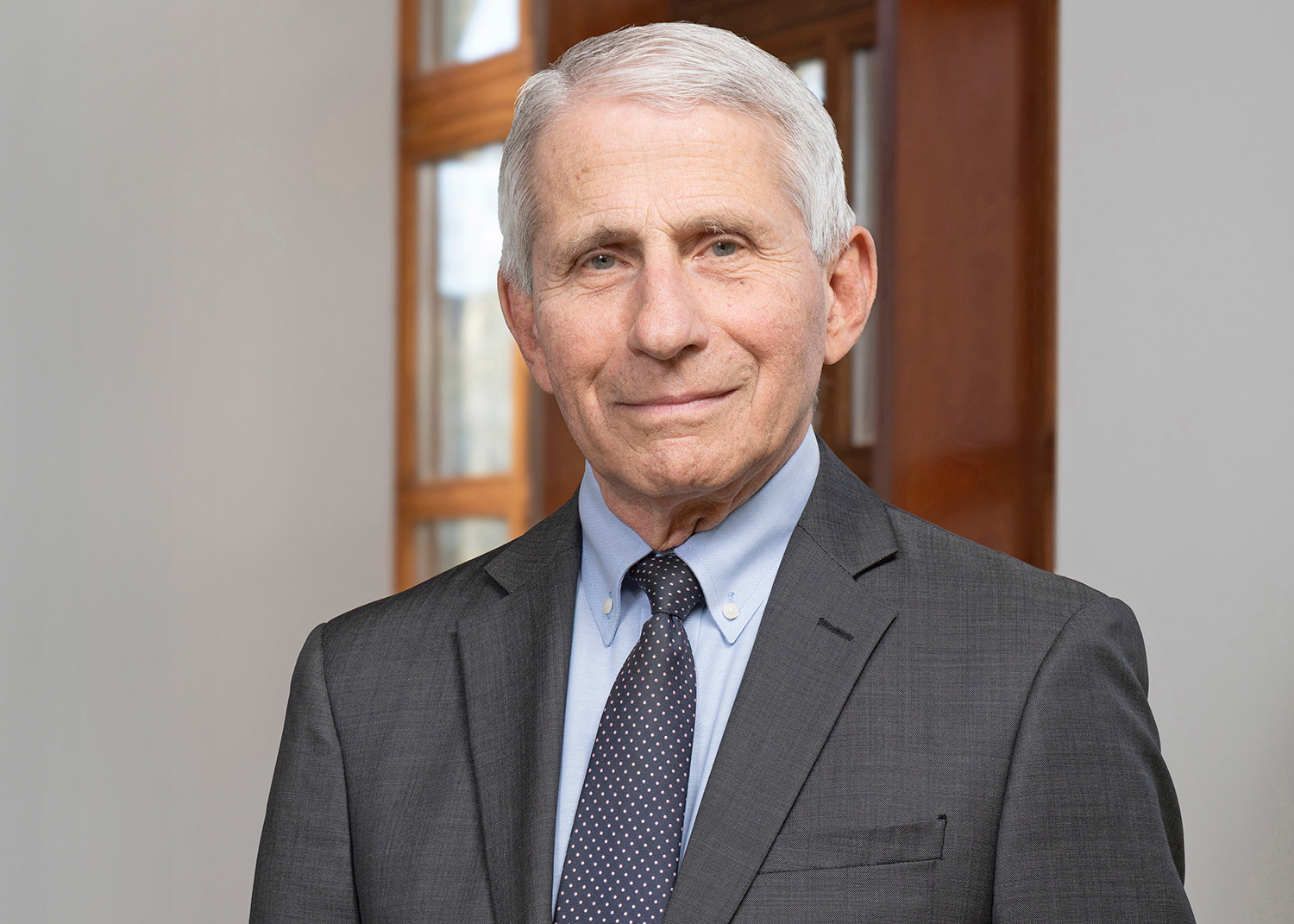 A photo of Dr. Anthony Fauci. He has short gray hair and is wearing a dark business suit and tie. He is looking at the viewer. 
