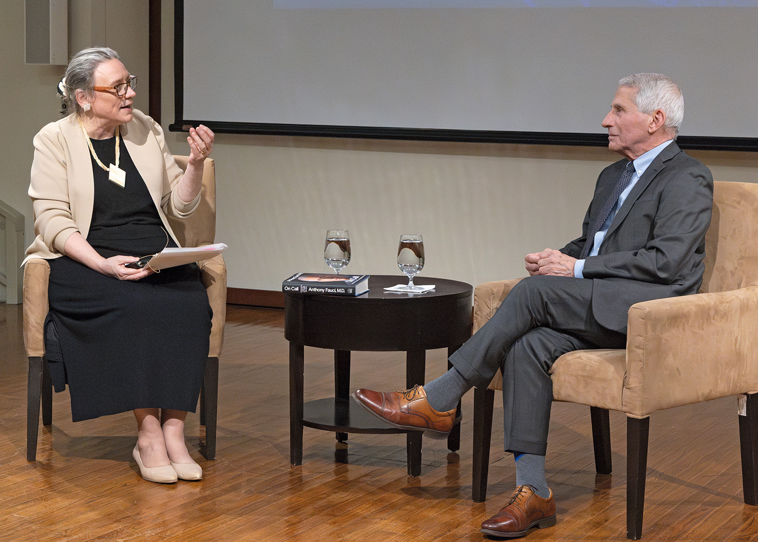 A photo of President Laurie Patton and Dr. Anthony Fauci in conversation. Both are seated in chairs, looking at each other. President Patton gestures with her left hand as she speaks to Dr. Fauci.