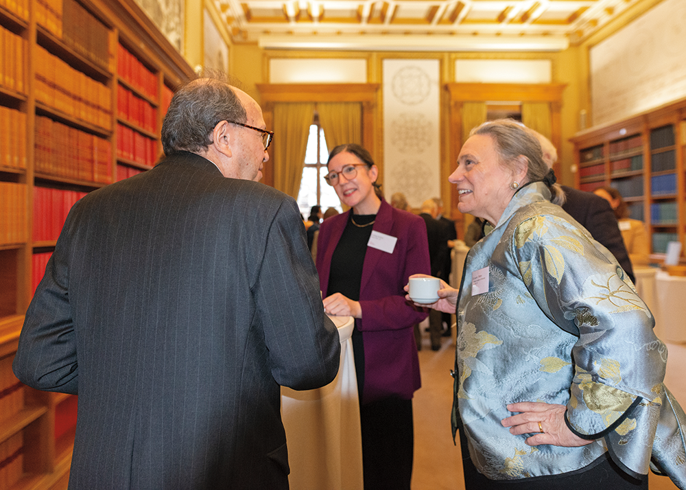 Three people are standing around a cocktail table, smiling and talking. All are wearing business attire.