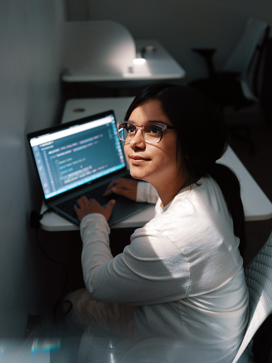 A woman looking up toward the light shining through a window while working on her laptop.