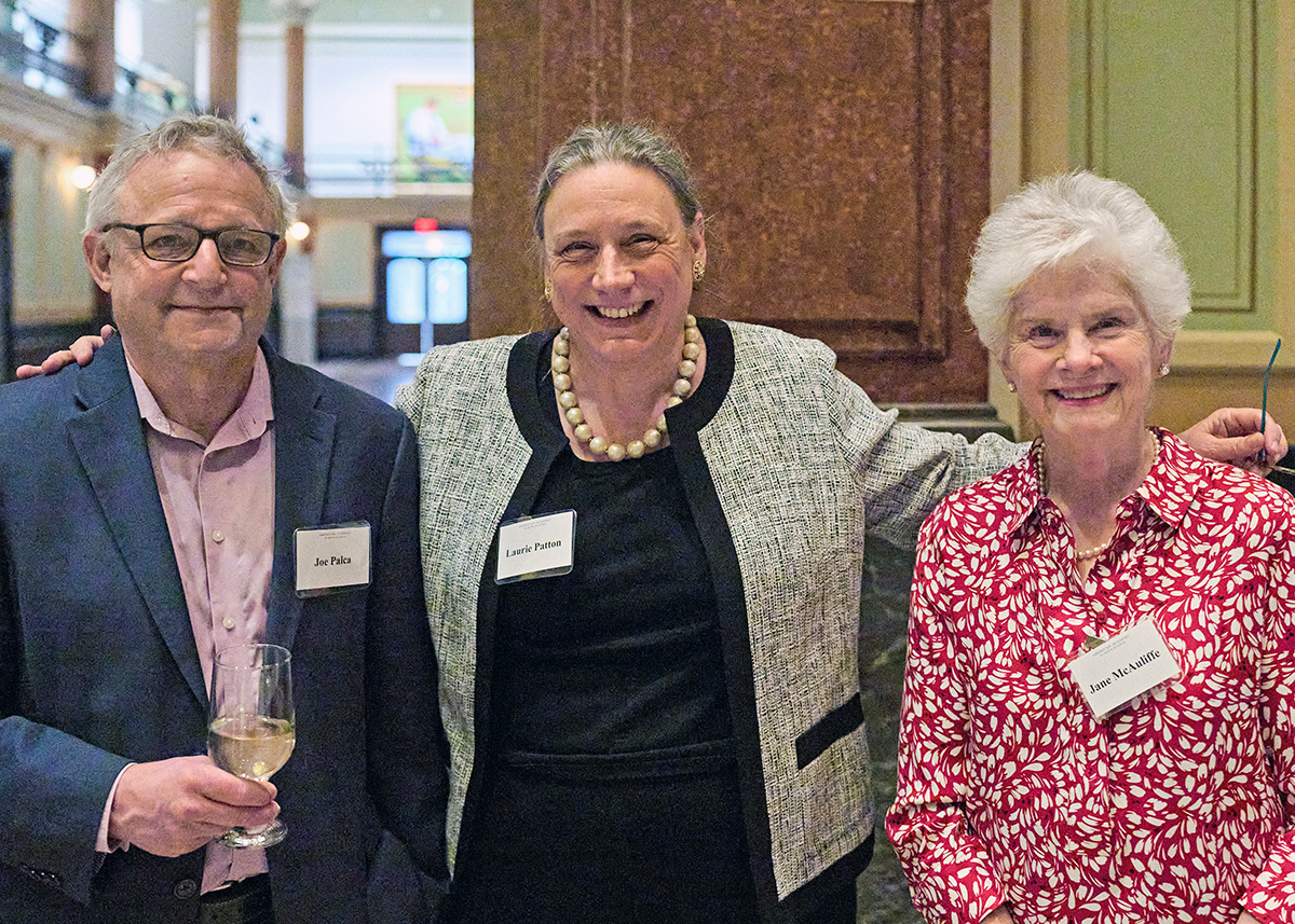 Three festively dressed adults pose and smile in an ornate lobby.