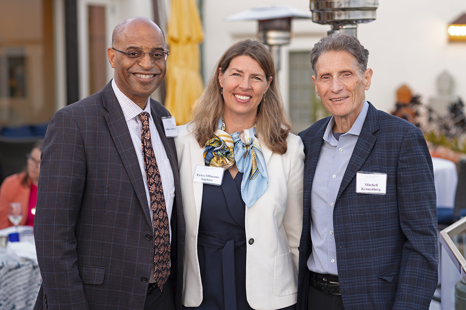 Three formally dressed adults pose at an outdoor reception. 