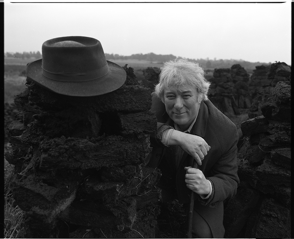 Seamus Heaney at a turf bog in Bellaghy wearing his father's coat, hat and walking stick and additional shots in the Bellaghy bog, 1986.  Bobbie Hanvey, photographer.