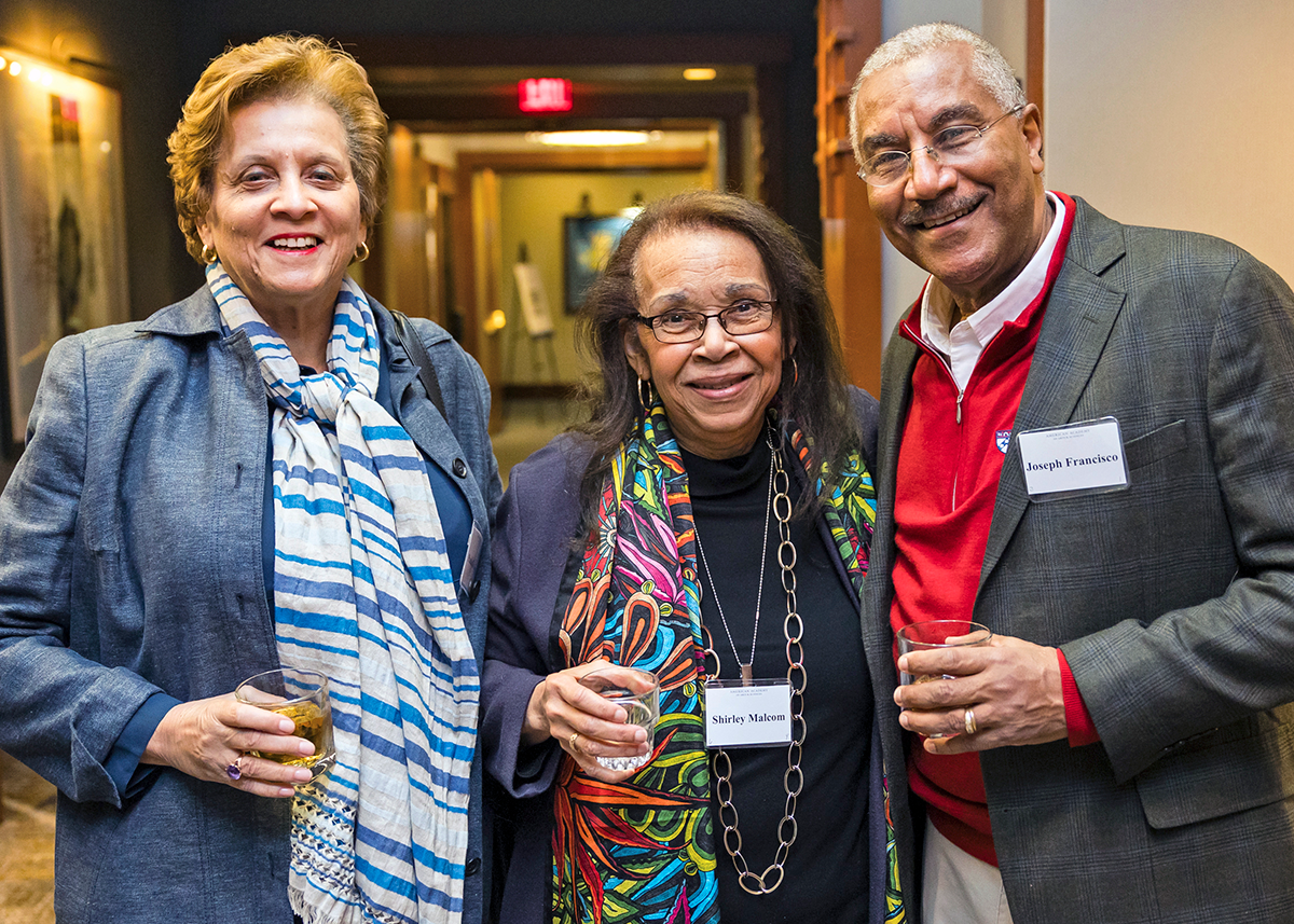Three festively dressed adults pose and smile at a reception. 