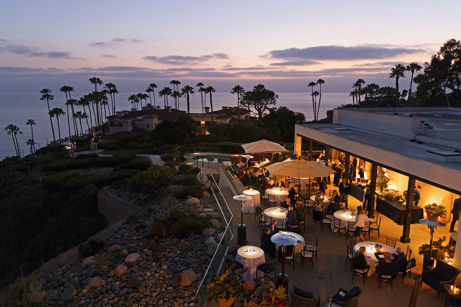 A wide shot of a cliffside patio overlooking the Pacific Ocean at night. 