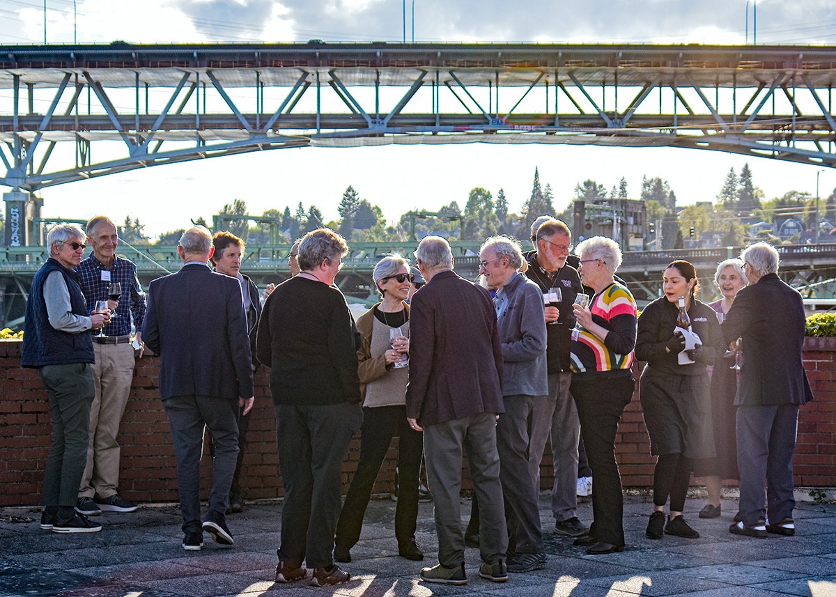 Well-dressed adults gather outdoors on a rooftop for a reception.
