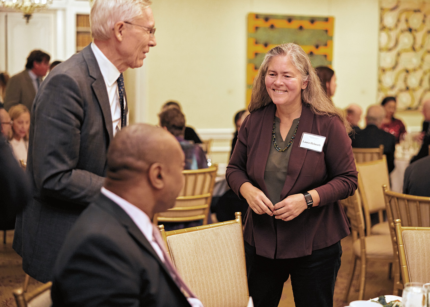 Three people talking together in a large dining room decorated with art.