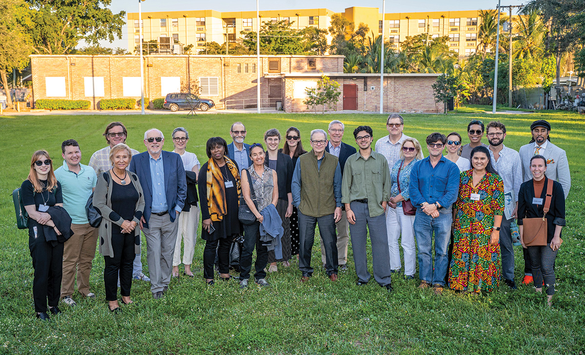 Two dozen of the members of the Commission on Accelerating Climate Action and project staff stand in a grassy expanse near a meeting hall.
