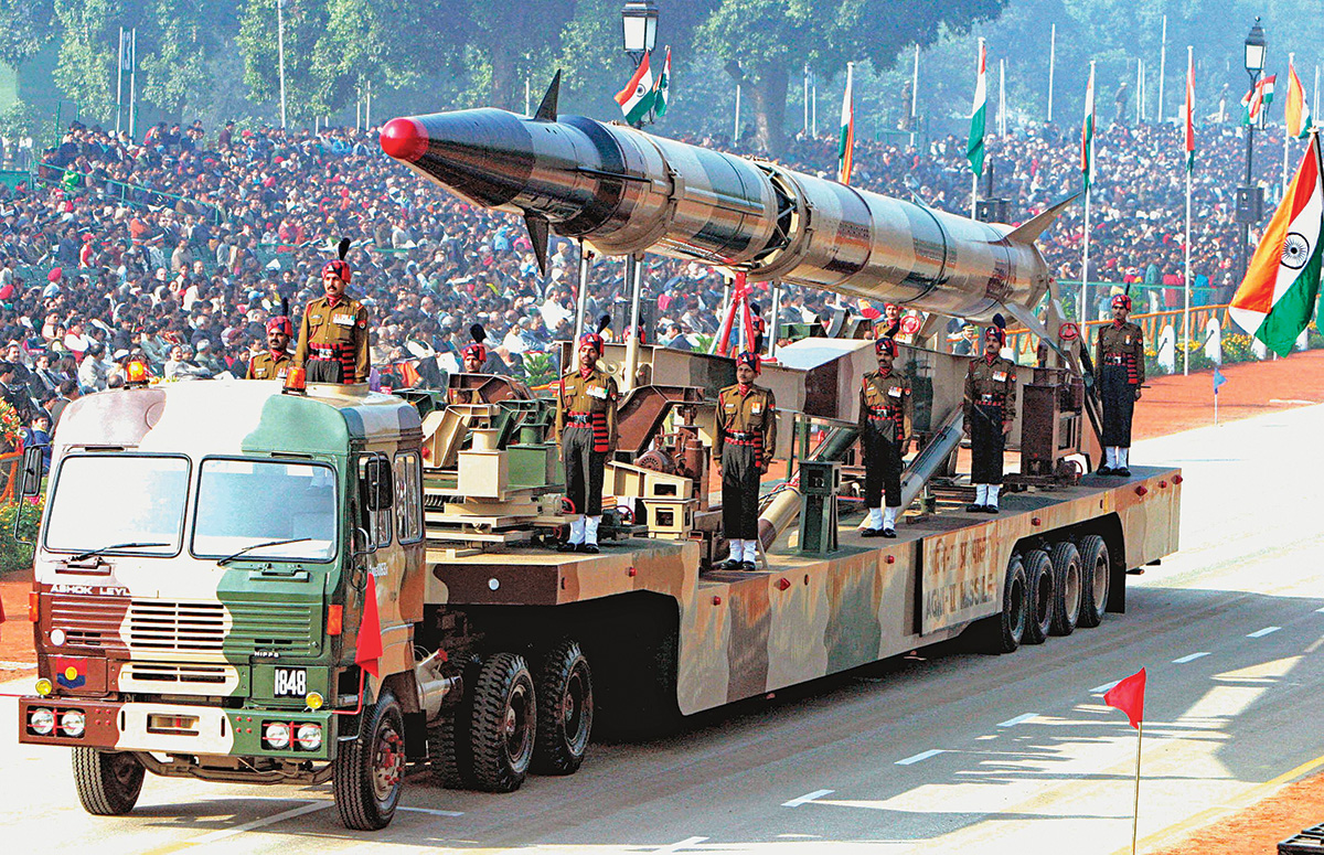 A trailer truck holds a large missile and several soldiers on its rig in a Republic Day parade in India. A sign below the missile reads “Agni-II Missile.”