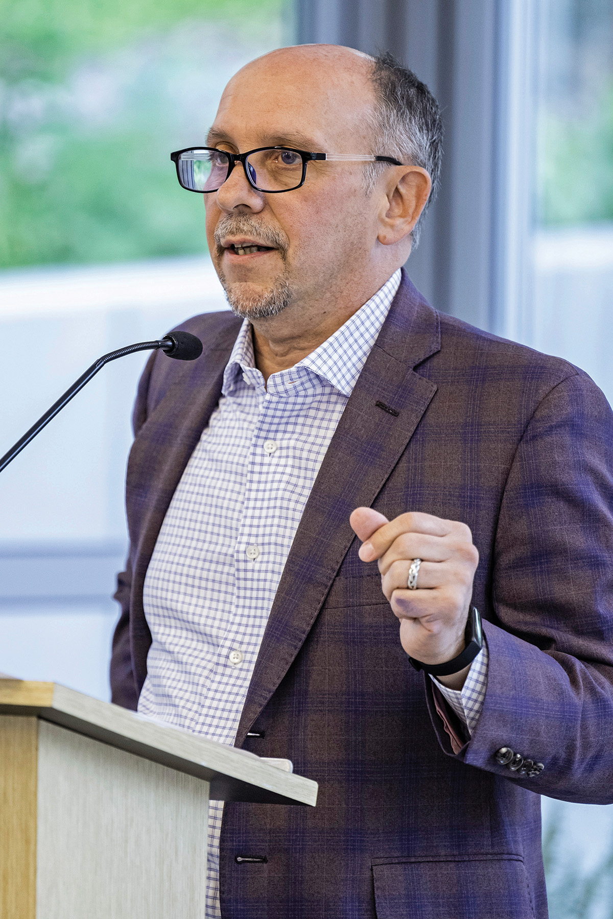 A photo of Jamie Merisotis, a person with pale skin and short graying hair. Merisotis wears a gray suit and glasses, and stands at a lectern with a microphone.
