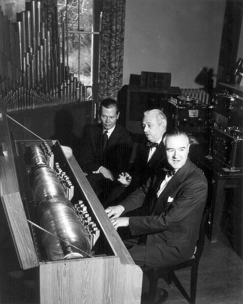 Three men are sitting in front of an armonica.