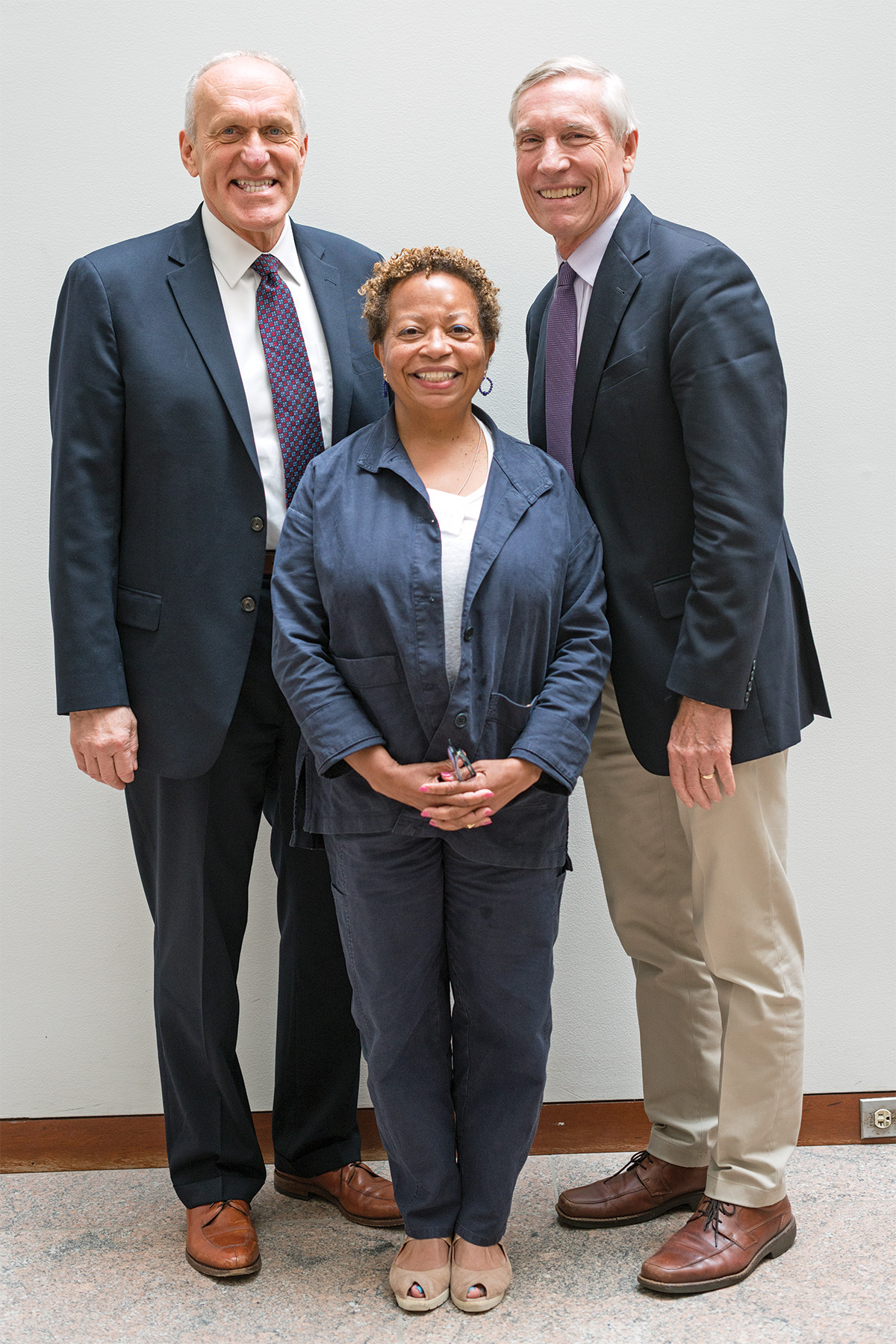 Three people face the viewer and smile. They each wear business attire.