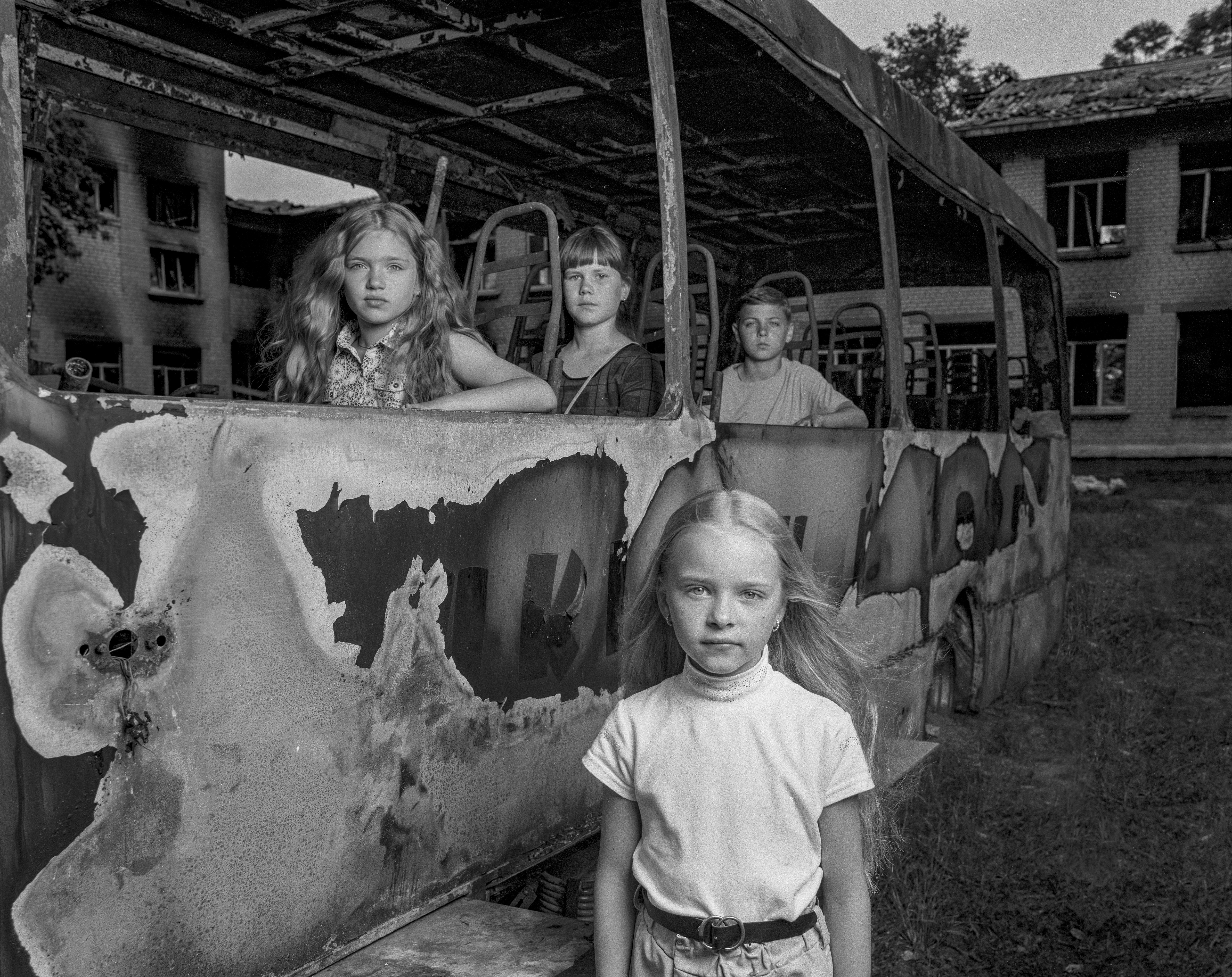 A black and white photo of children inside and near a school bus in Kyiv, Ukraine that was irreparably damaged by Russia's army.