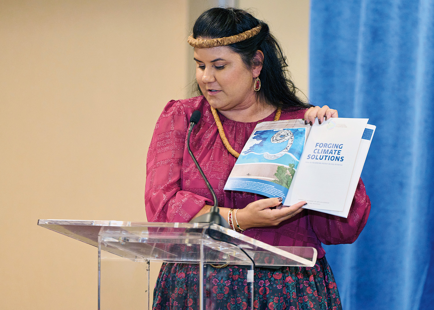 A woman standing at a podium holding open a report to show an image to the audience.
