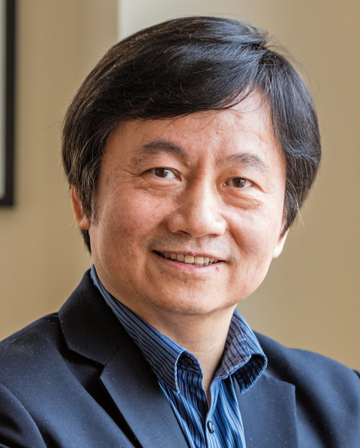 A headshot of Francis Amory Prize recipient Haifan Lin, a person with short, dark hair and pale skin. Lin wears a dark blue blazer and striped dress shirt, while smiling at the viewer. 