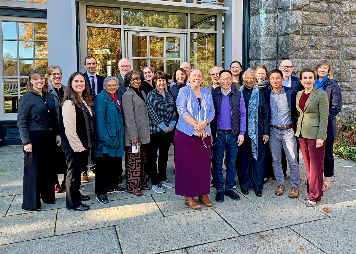 A group of people standing together, smiling outside in front of a brick building.