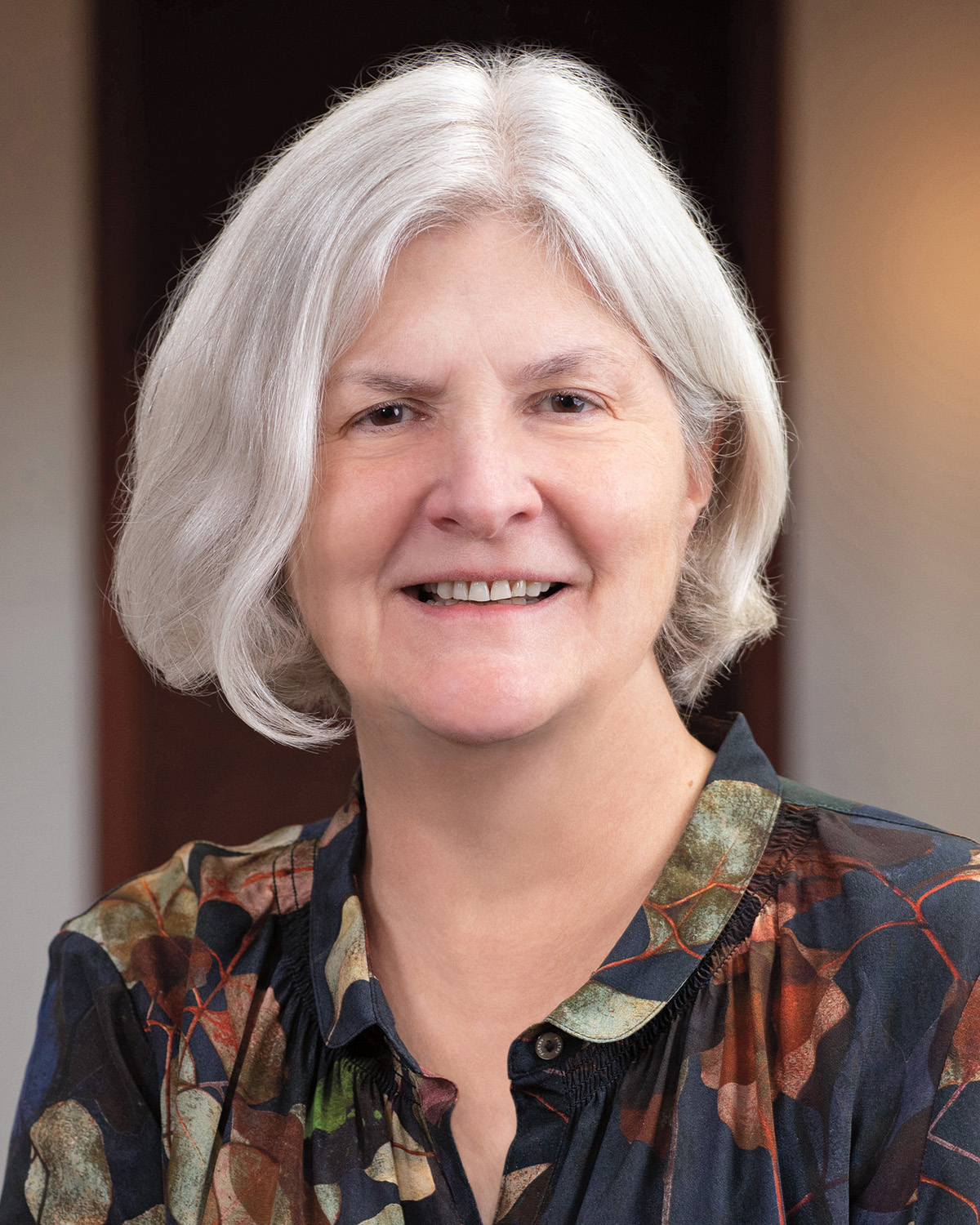 A headshot of Nancy C. Andrews, who has pale skin and shoulder-length white hair. She faces the viewer and smiles.