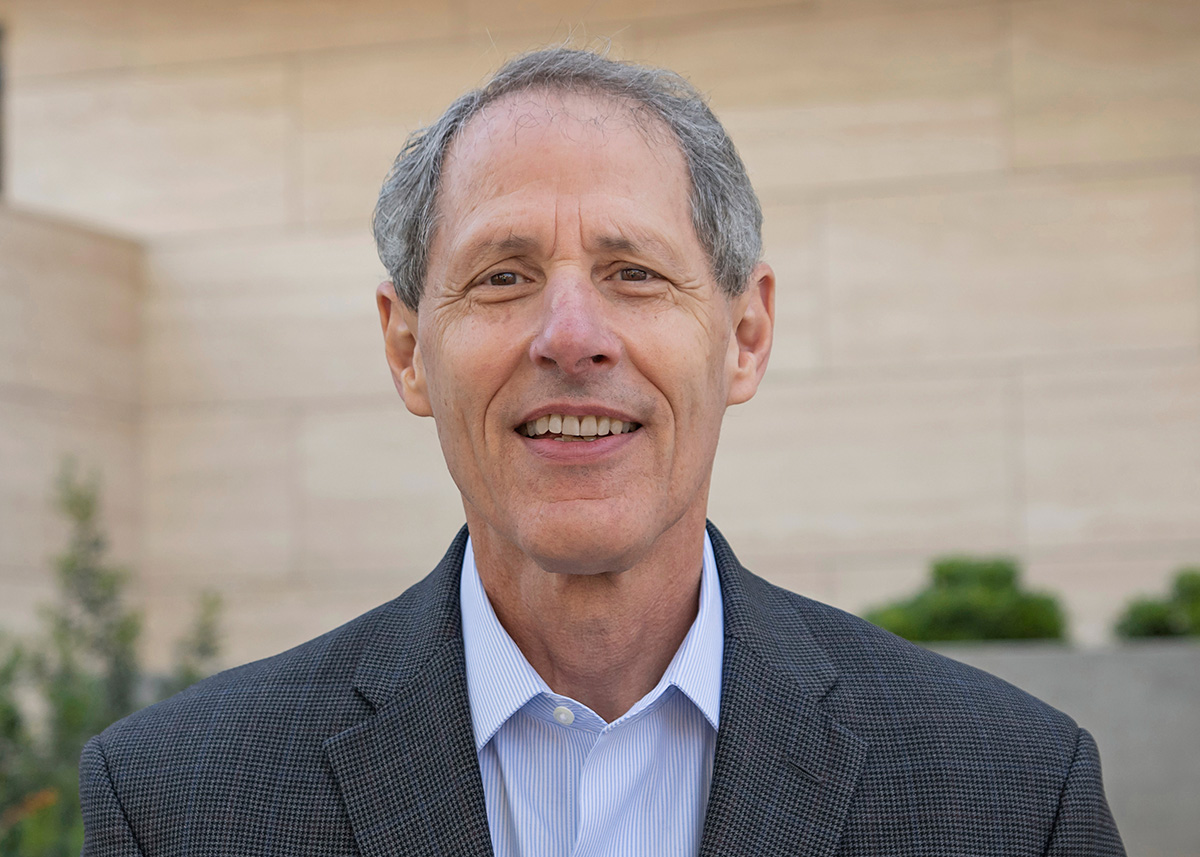 A photograph of a light-skinned man with short gray hair. He is wearing business attire and looking toward the viewer. 