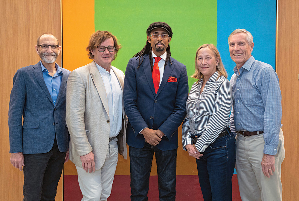 Five people in business attire stand smiling in front of a colorful painting.  