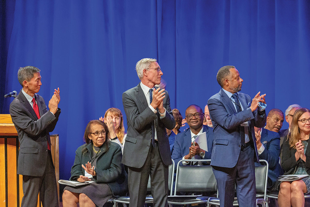 Goodwin Liu and David Oxtoby stand and applaud in front of the assembled speakers during the 2023 Induction ceremony.