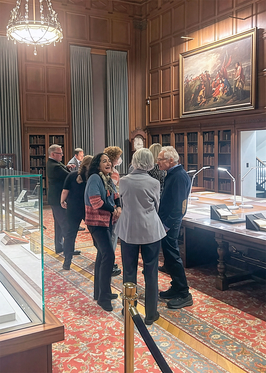 Adults mingle in a formal library setting among museum display cases. 