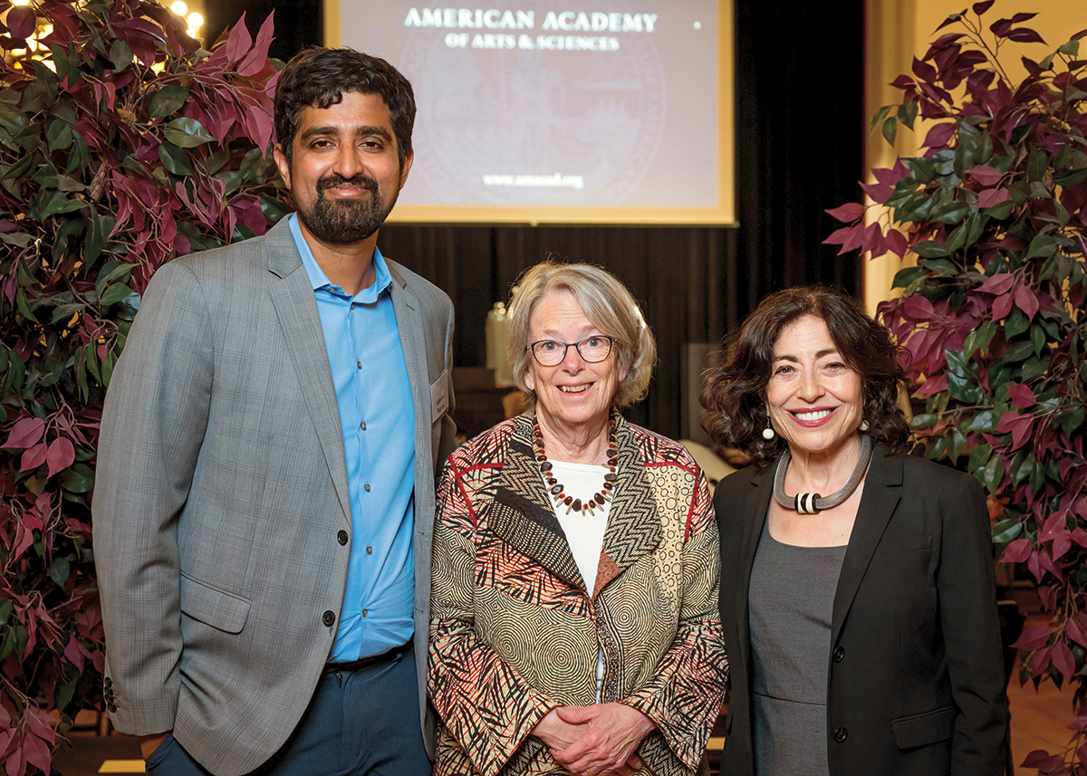 Three formally dressed panelists pose and smile. 