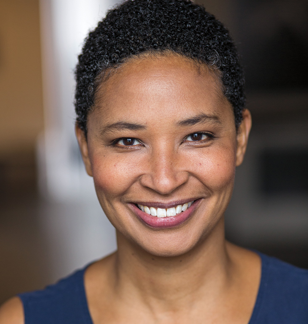 A headshot of Danielle Allen wearing a sleeveless blue shirt. Allen has brown skin, brown eyes, and short curly black hair. She faces the viewer and smiles. 