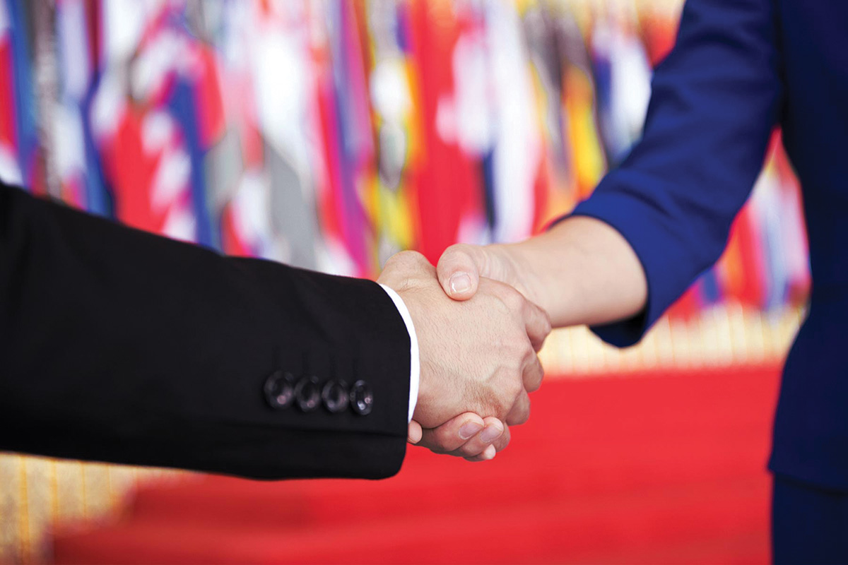 A close-up of two arms extending to meet and shake hands in the center of the image.