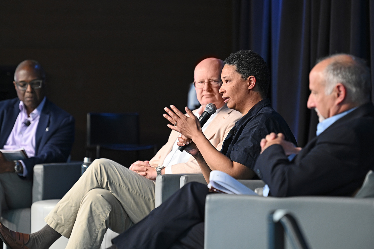 Four adults sitting on stage for a panel; one panelist is holding a microphone. 