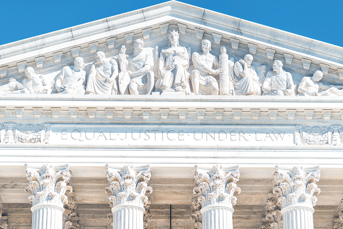 The relief sculptures on the pediment of Supreme Court Building on a sunny day. Beneath the states are the words “Equal Justice Under Law.”