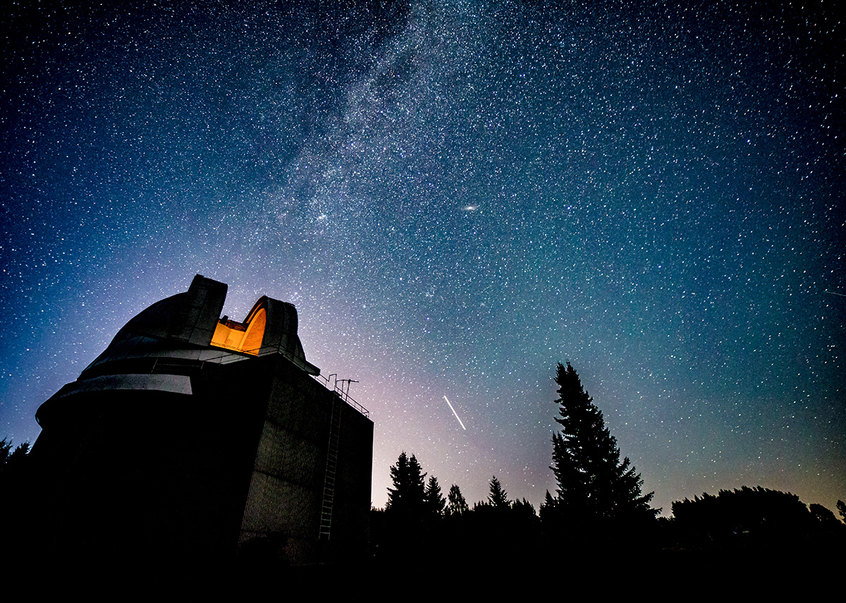 A view of the Milky Way galaxy at night seen over the open dome of an observatory. 