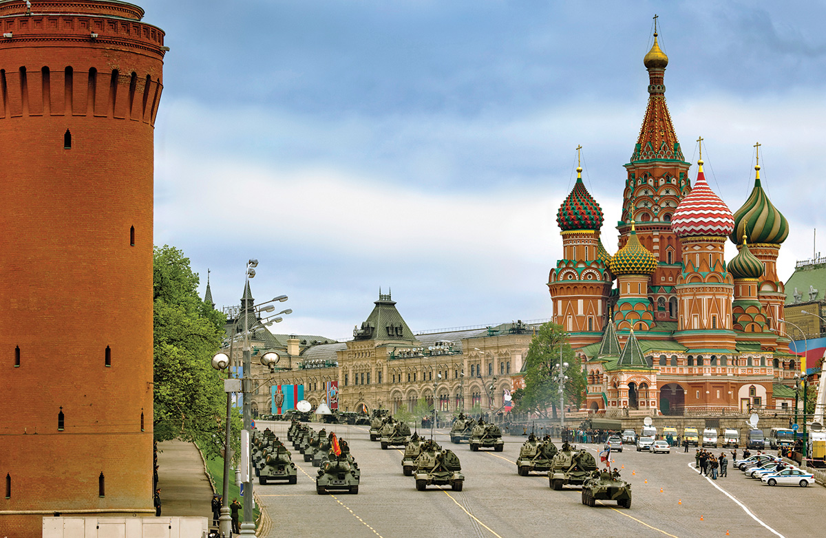 A military parade fills a four-lane road to mark Soviet Victory Day in Moscow. The road is beside an Orthodox church with ornate minarets.