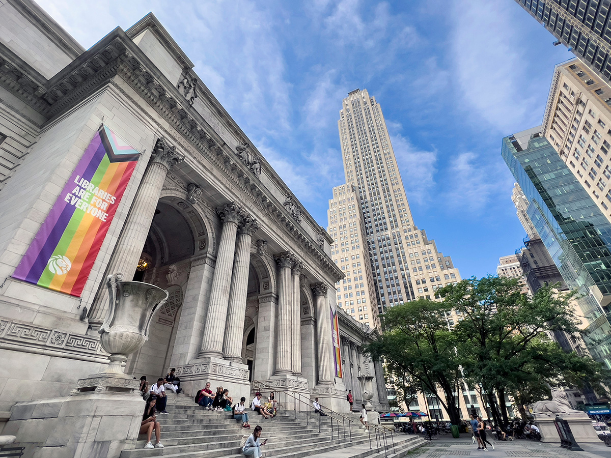 A view of the steps of the main branch of the New York Public Library, with a large banner on the building reading “Libraries are for everyone.”