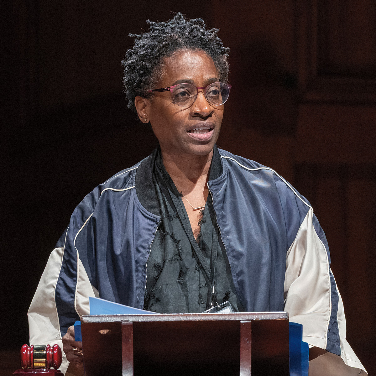 A photo of Jacqueline Woodson, a person with dark skin and dark curly hair.&nbsp; She is wearing glasses and a blue jacket and top and is speaking at a podium.