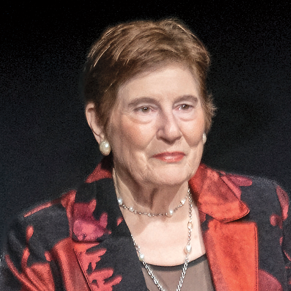 A woman with short brown hair, wearing a red and black jacket, is facing the viewer.