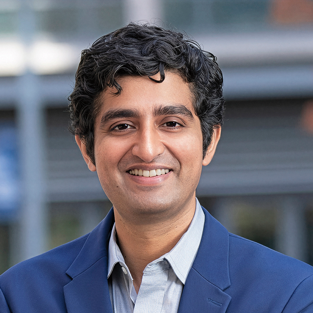 A man wearing a blue jacket and a white shirt is smiling for the camera.