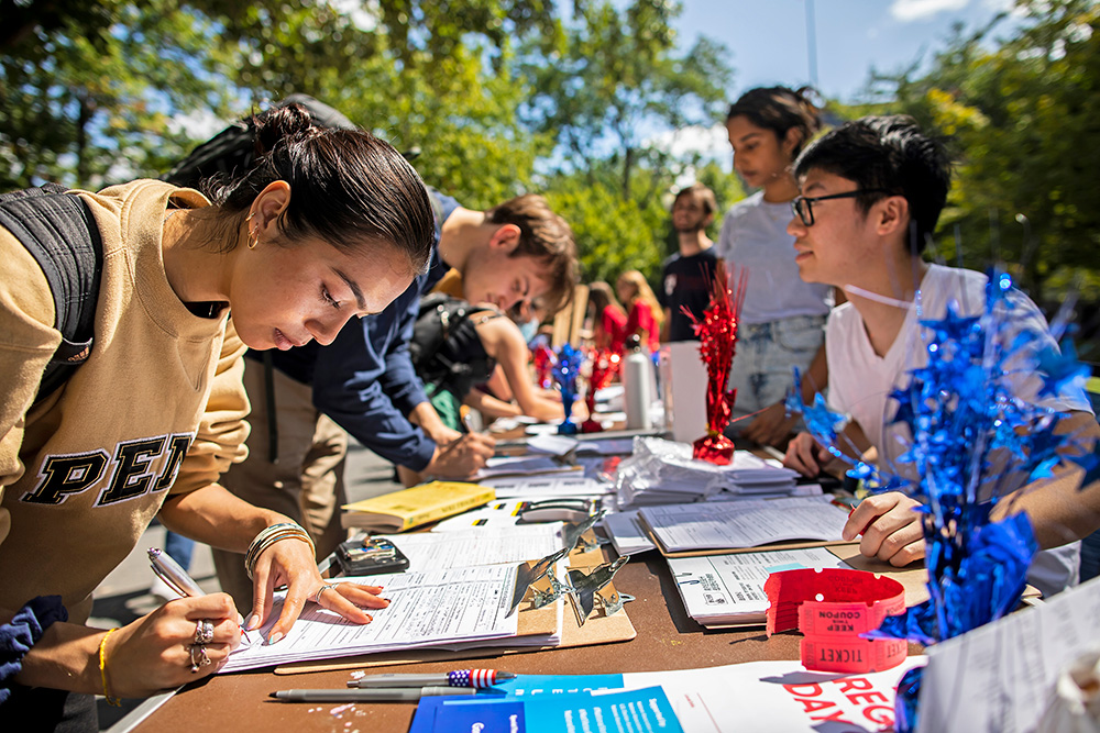 Students at an undisclosed university stand around a table with clipboards and sign up to participate in campus activities.