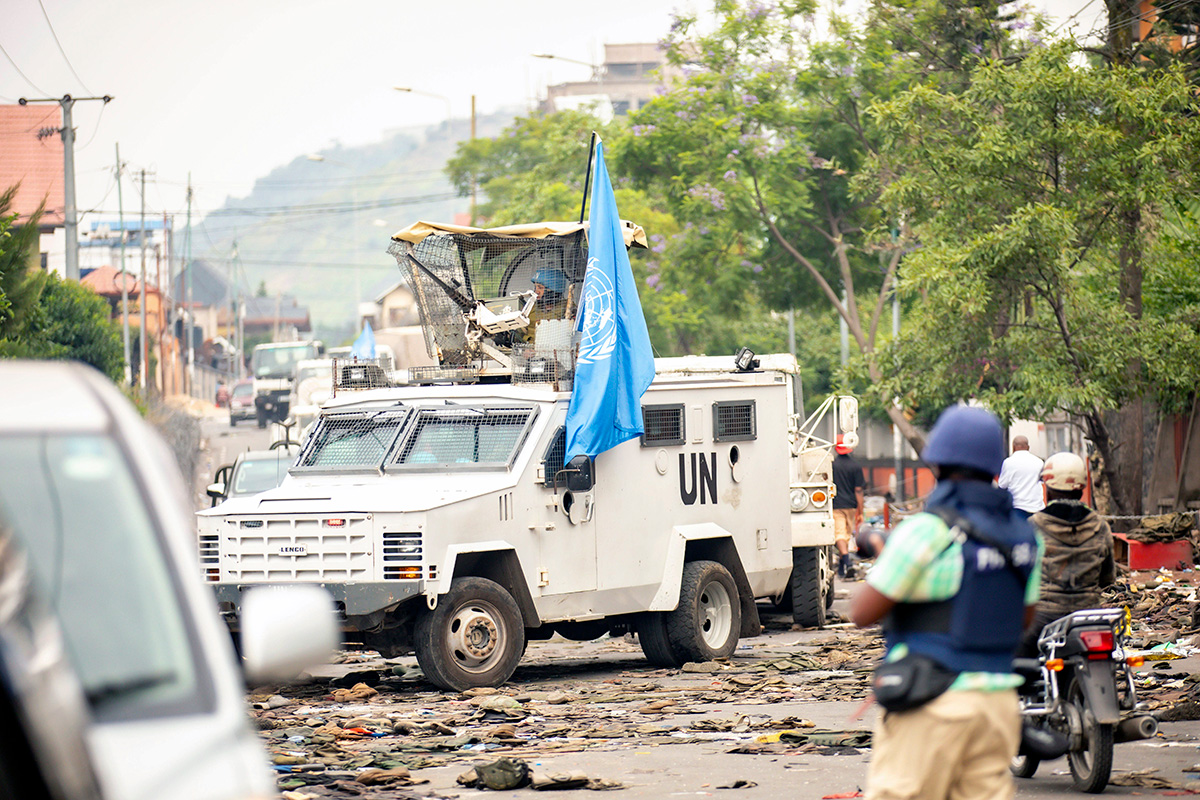 An armored vehicle, carrying the flag of the United Nations and with the letters UN on its side, drives through an urban conflict zone in Goma. 