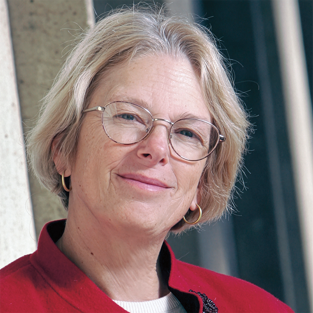 A woman wearing a red jacket and glasses is smiling for the camera.