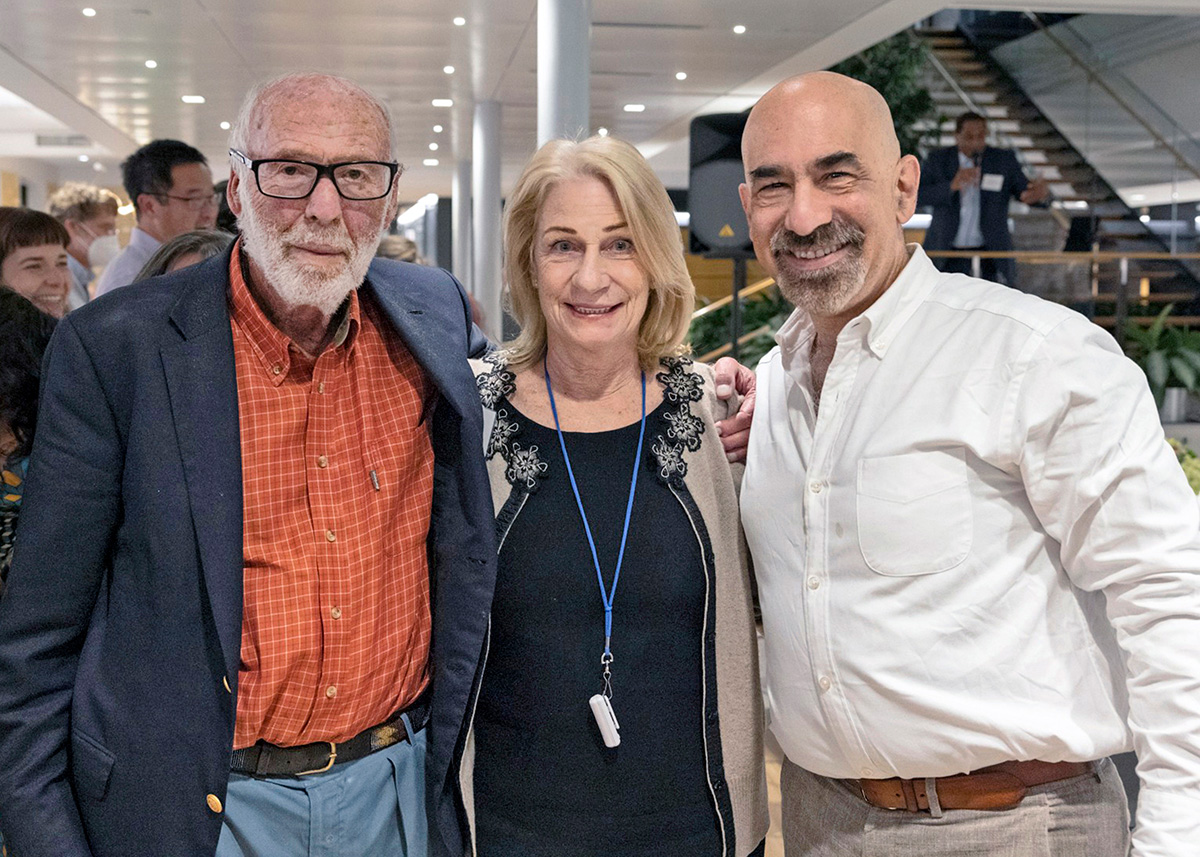 A photograph of three individuals who are standing shoulder to shoulder and all looking toward the viewer. 